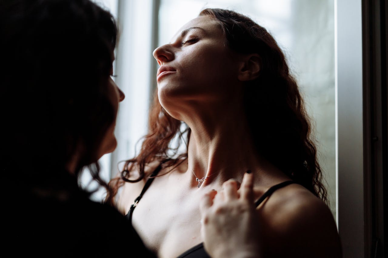 Close-up of two women embracing, capturing an intimate and romantic moment by the window in soft lighting.
